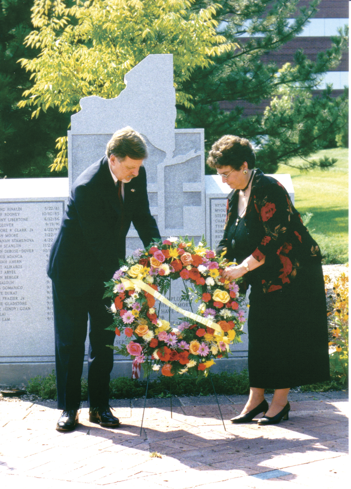 Roger Benson and a woman lay a wreath in front of a 9/11 memorial.